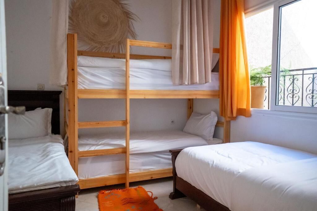 A room with a bunk bed, a single bed, and a window with curtains.