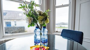 A glass table with a vase of flowers, two water bottles, and a packet of snacks.