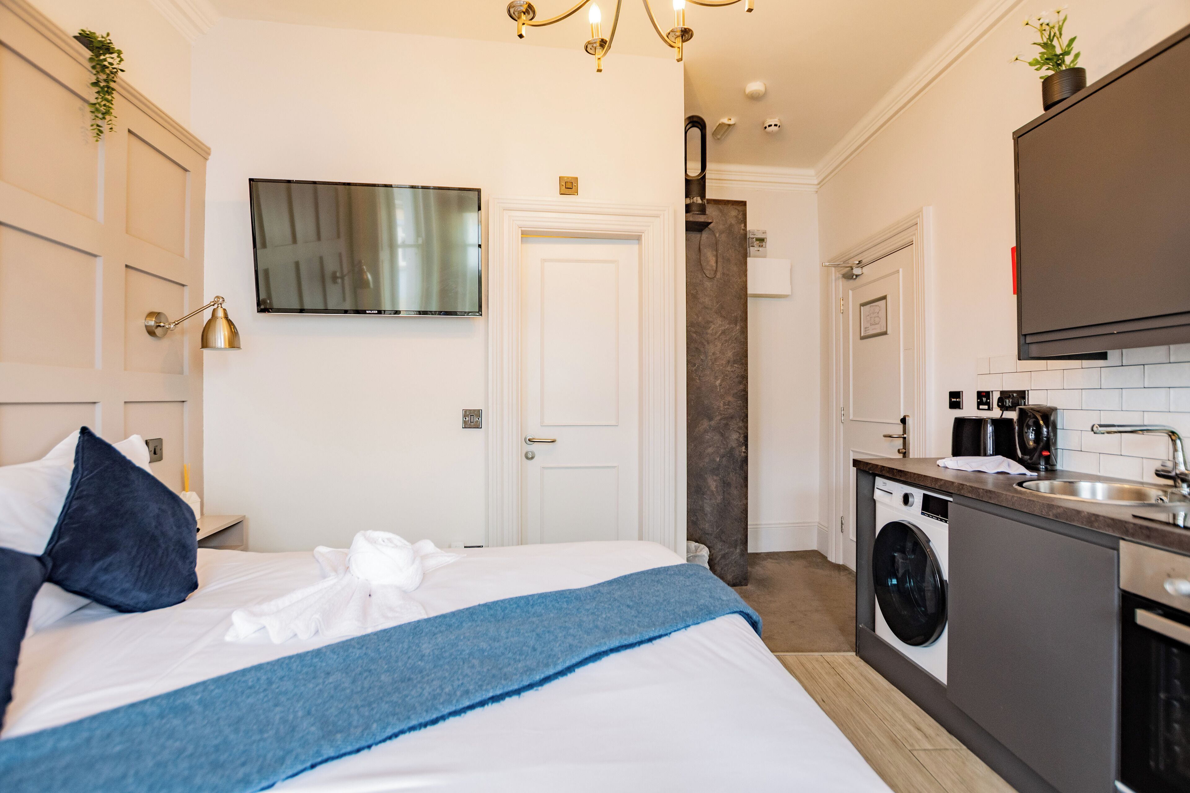 Une chambre d’hôtel équipée d’un lit, d’une machine à laver, d’un lavabo et d’un téléviseur fixé au mur.