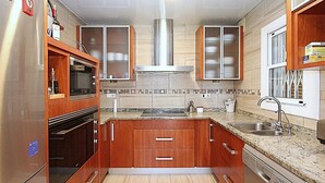 Une cuisine avec des meubles de rangement en bois, un réfrigérateur en acier inoxydable, un four encastré, un four à micro-ondes, une cuisinière à gaz, un évier et une fenêtre.