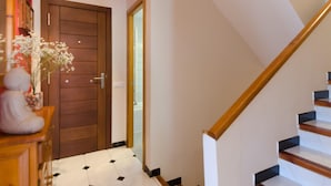 Un couloir menant à un escalier, avec une porte en bois et un sol carrelé de carreaux blancs.