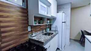 Eine Küche mit Holzwand, einer Mikrowelle, einem Spülbecken und einem Kühlschrank.