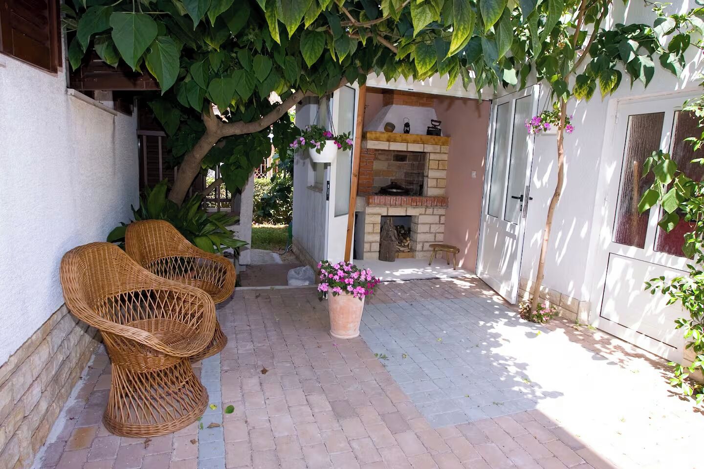 Une terrasse avec des chaises en osier, une plante en pot et une cheminée en briques.