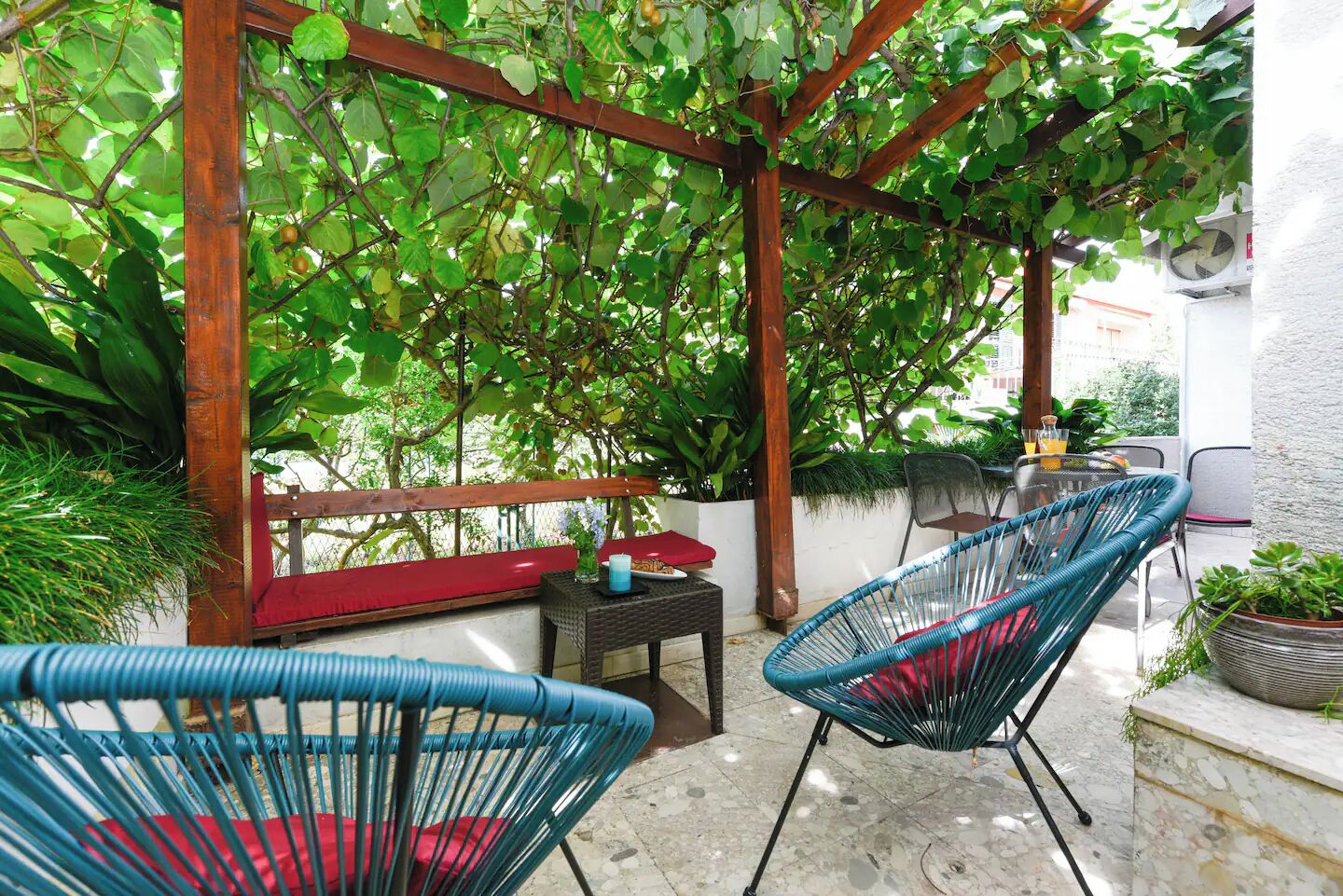 A covered outdoor seating area with wicker chairs, a table, and a bench.