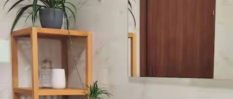 A modern bathroom with a white vanity, a wooden shelf with plants, and a mirror above the sink.