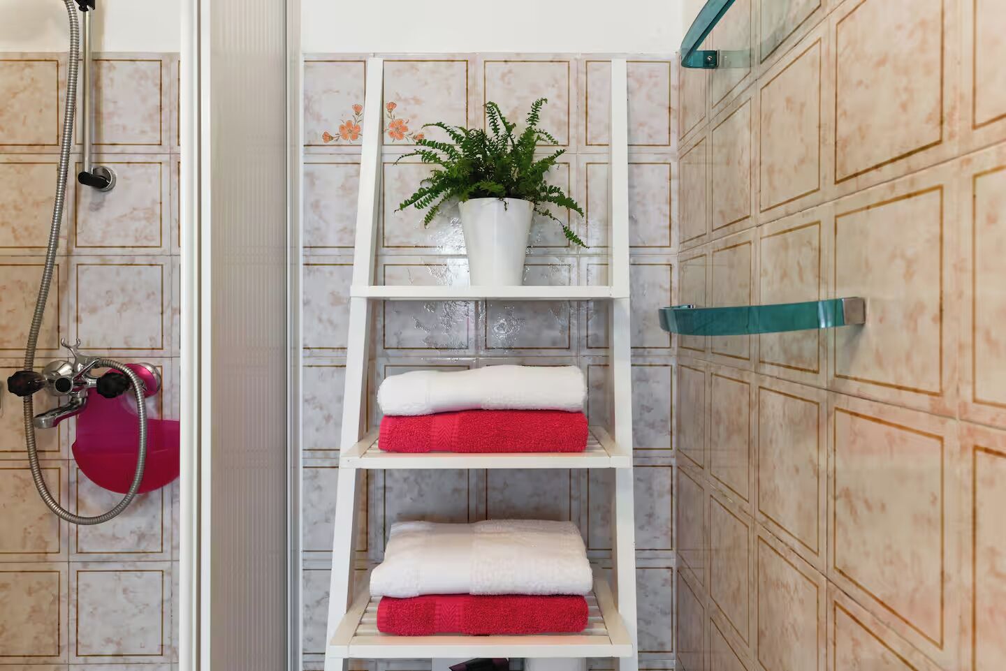 A bathroom with a shower, a white shelf with towels, and a potted plant.