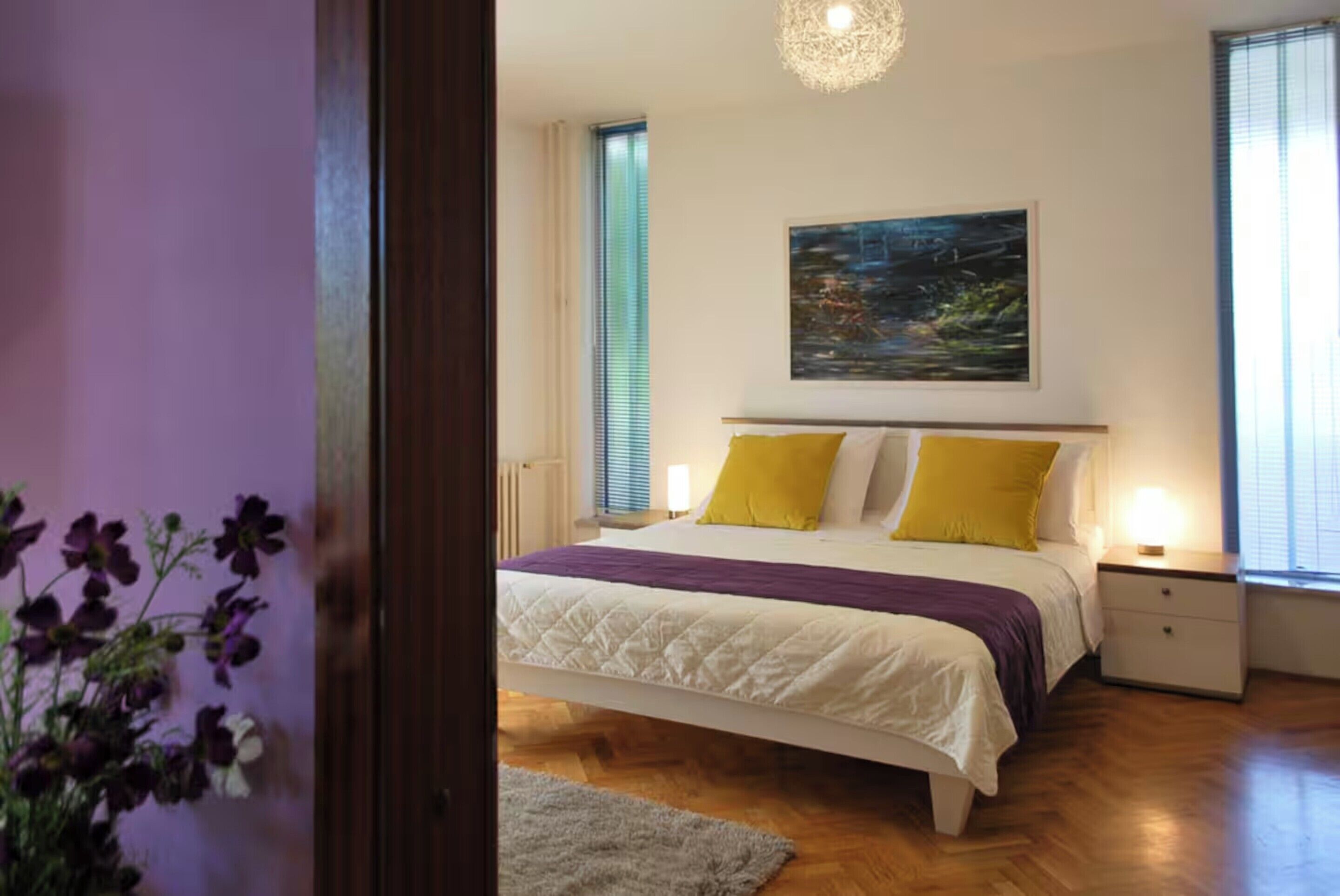 Ein Schlafzimmer mit Bett, Nachttischen, einem Bild an der Wand und einem Fenster mit Jalousien.