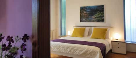 A bedroom with a bed, bedside tables, a painting on the wall, and a window with blinds.