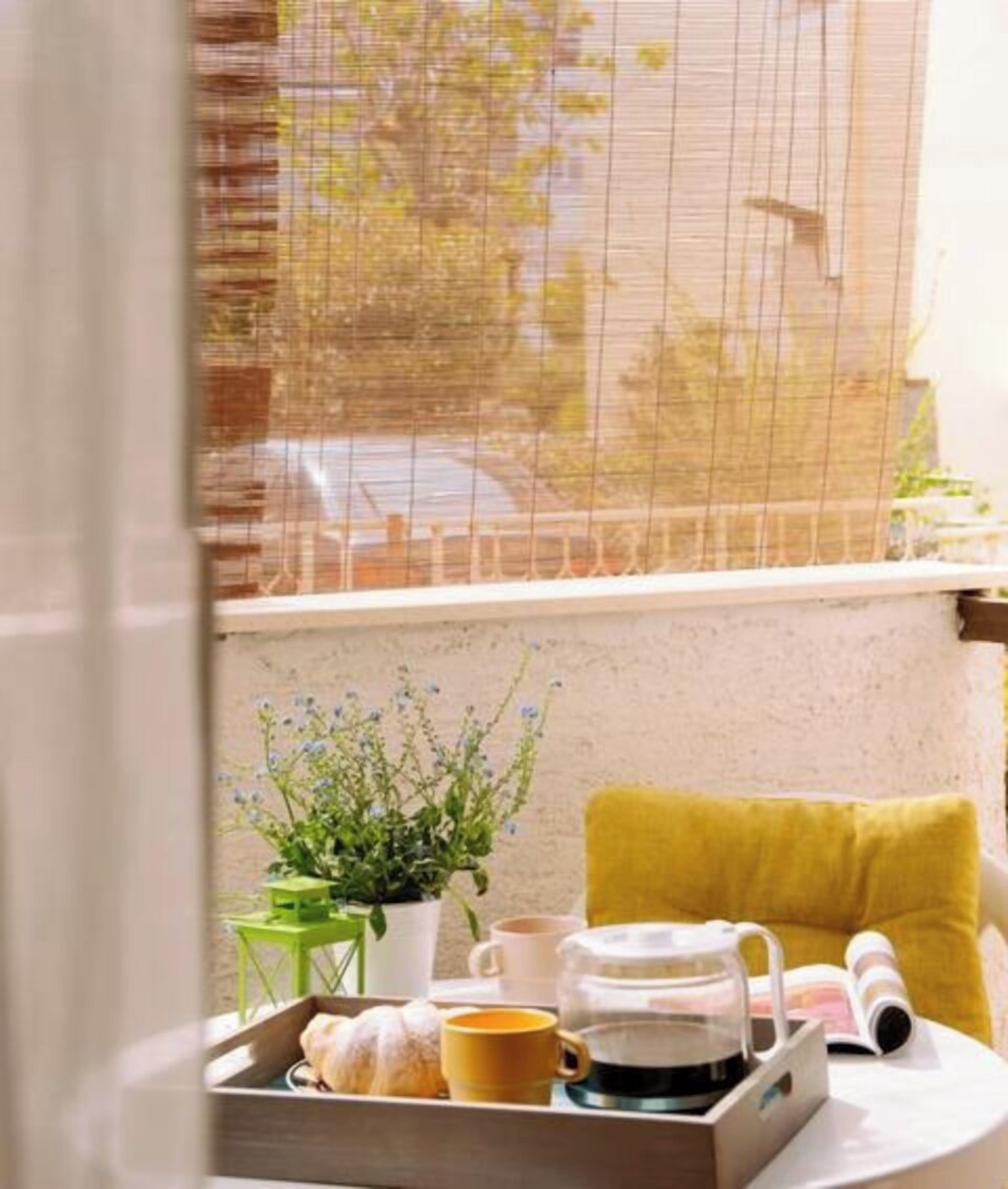 Une fenêtre donnant sur une rue, une petite table avec un plateau de nourriture, une tasse, une théière et une plante.