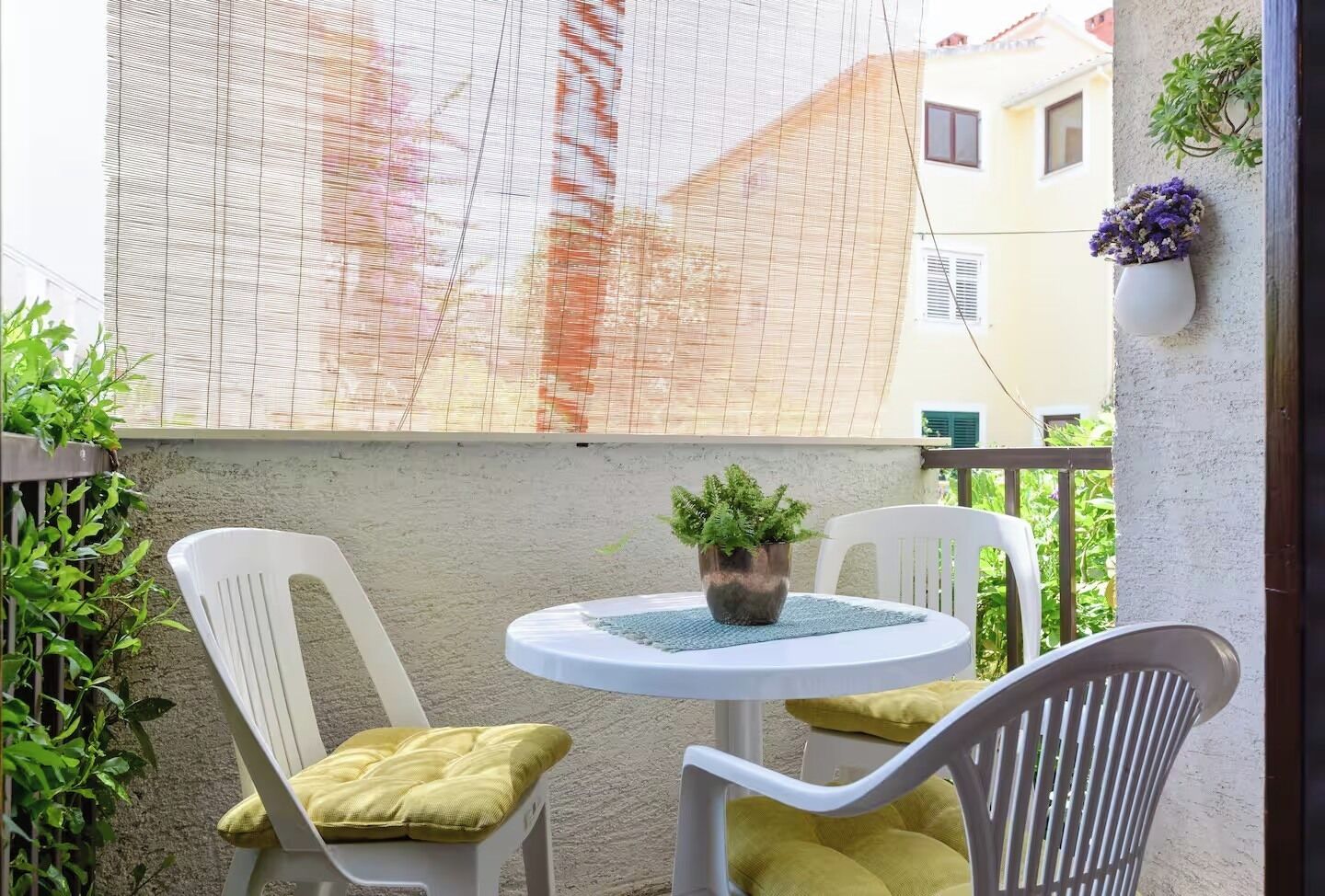 A balcony with a table and two chairs, a potted plant, and a wall-mounted planter with flowers.