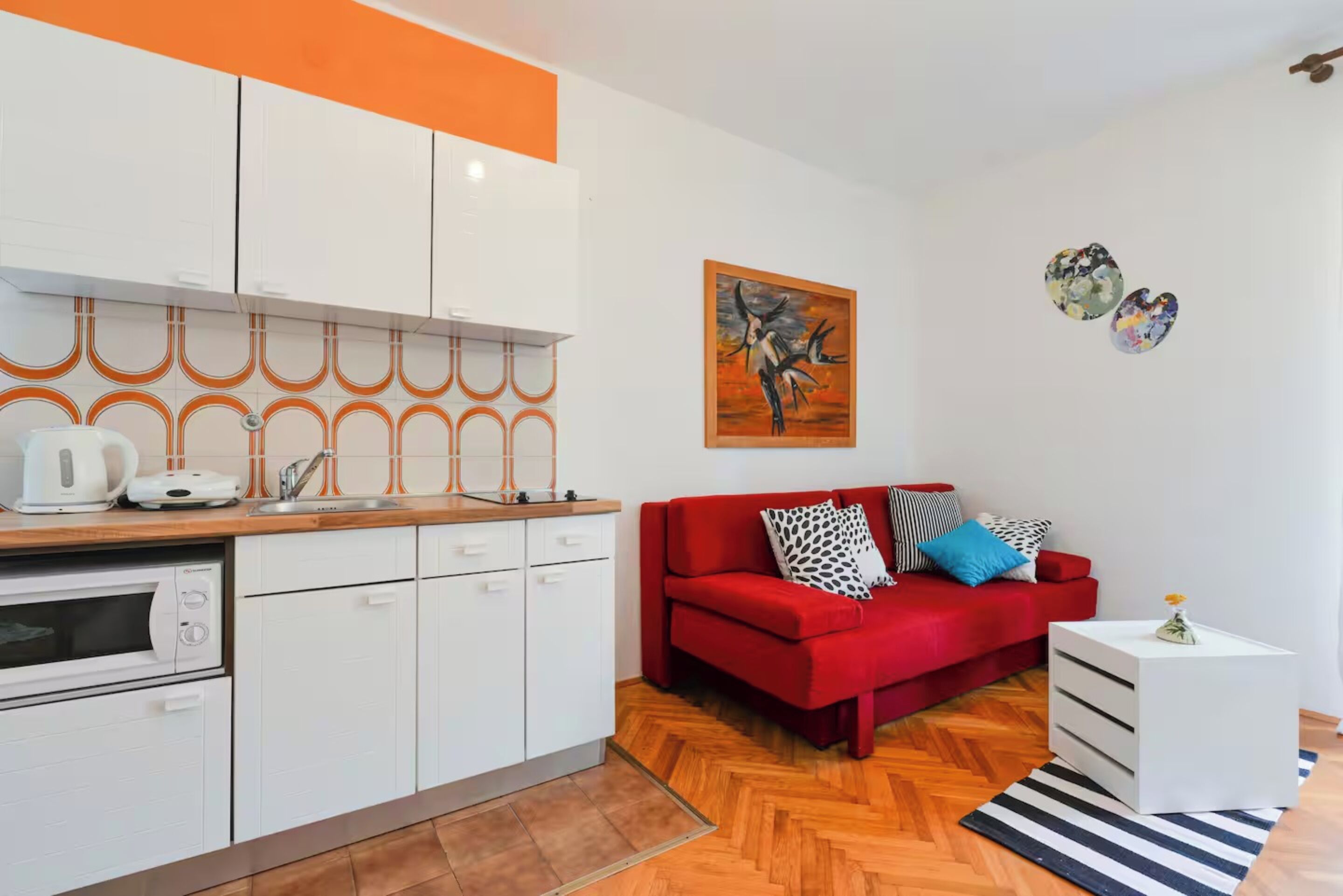 A modern kitchen with white cabinets, a red sofa, and a painting on the wall.