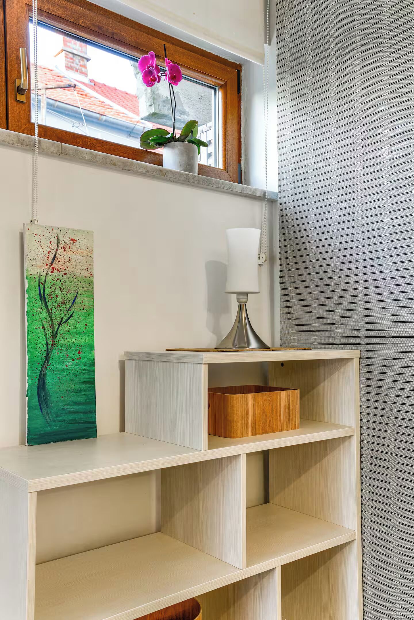 A room with a window, a painting, a lamp, and a shelf.