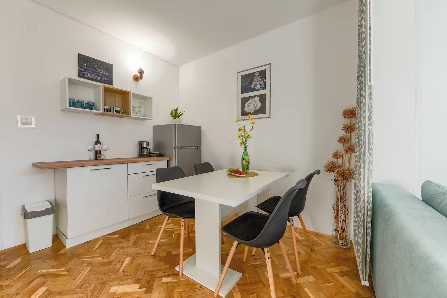 A compact kitchen with a dining area, a refrigerator, a coffee maker, and a vase with flowers.