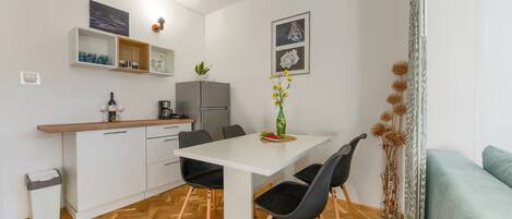A compact kitchen with a dining area, a refrigerator, a coffee maker, and a vase with flowers.