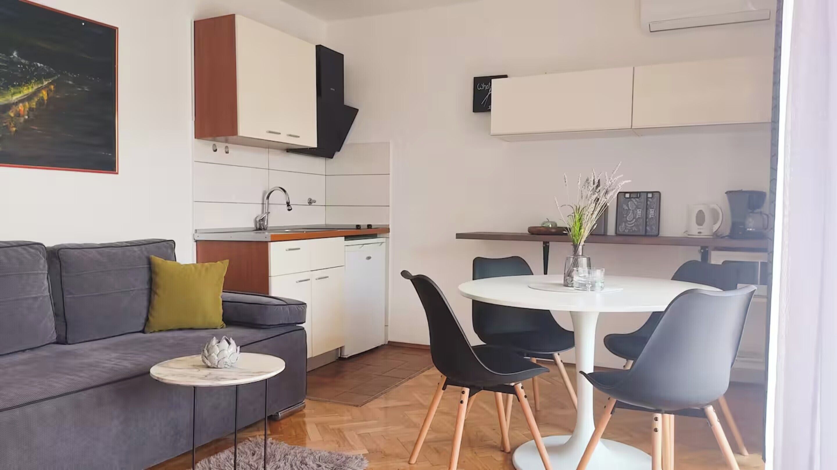 A compact living space with a sofa, a dining table with chairs, a small kitchen area, and a painting on the wall.