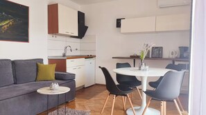 Un espacio habitable pequeño con un sofá, una mesa de comedor con sillas, una cocina compacta y un cuadro en la pared.