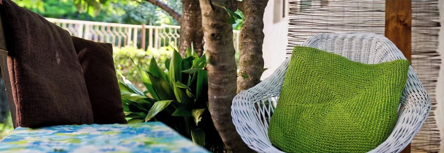 Uma cadeira de vime com um travesseiro verde, um travesseiro marrom e um travesseiro azul estampado sobre uma mesa.