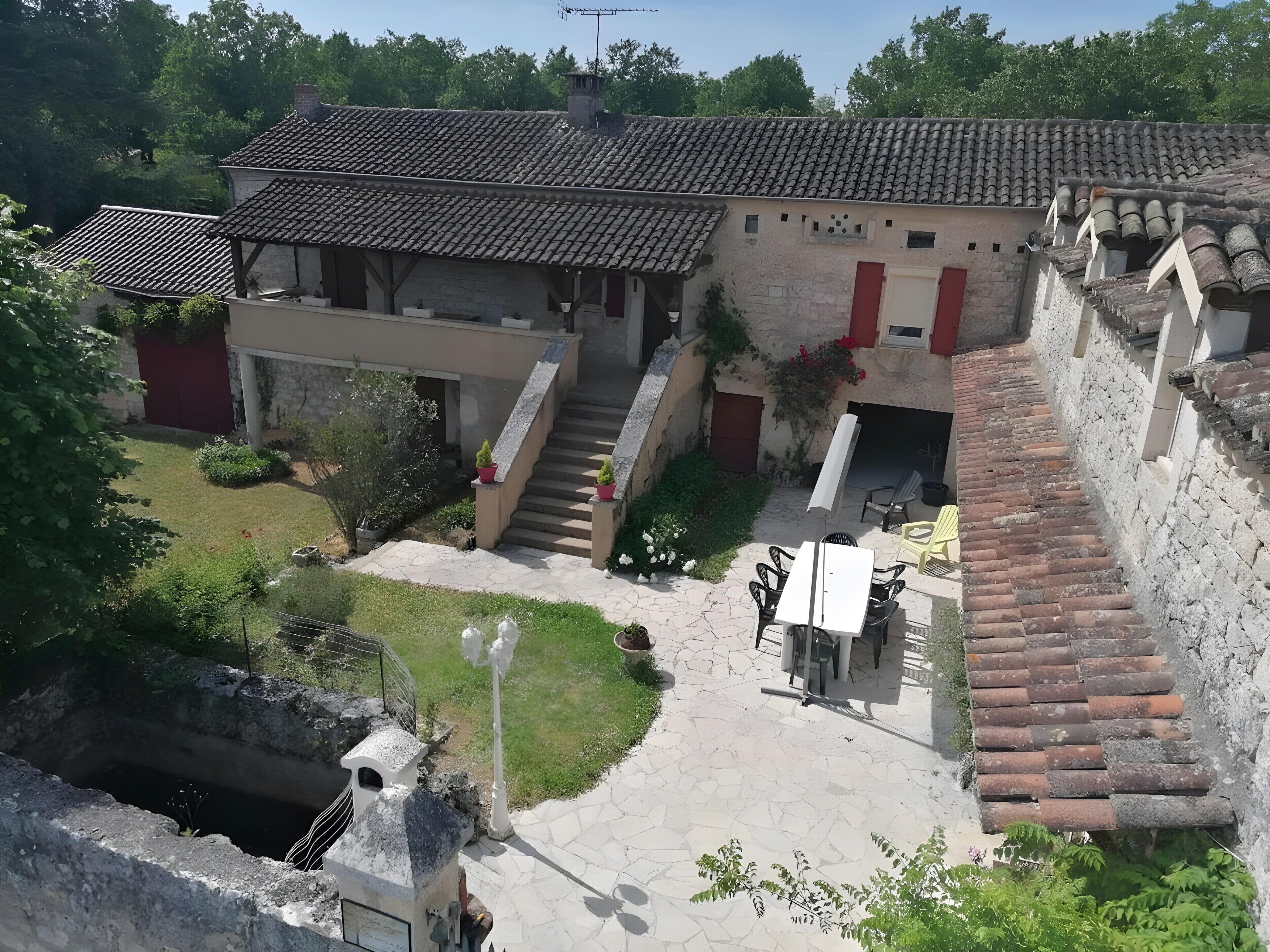 A courtyard with a stone staircase, a white building with red shutters, and a small outdoor seating area.