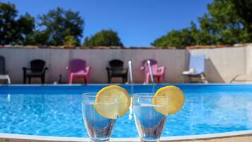 Una piscina con dos vasos de agua y rodajas de limón, rodeada de sillas y un cielo despejado.