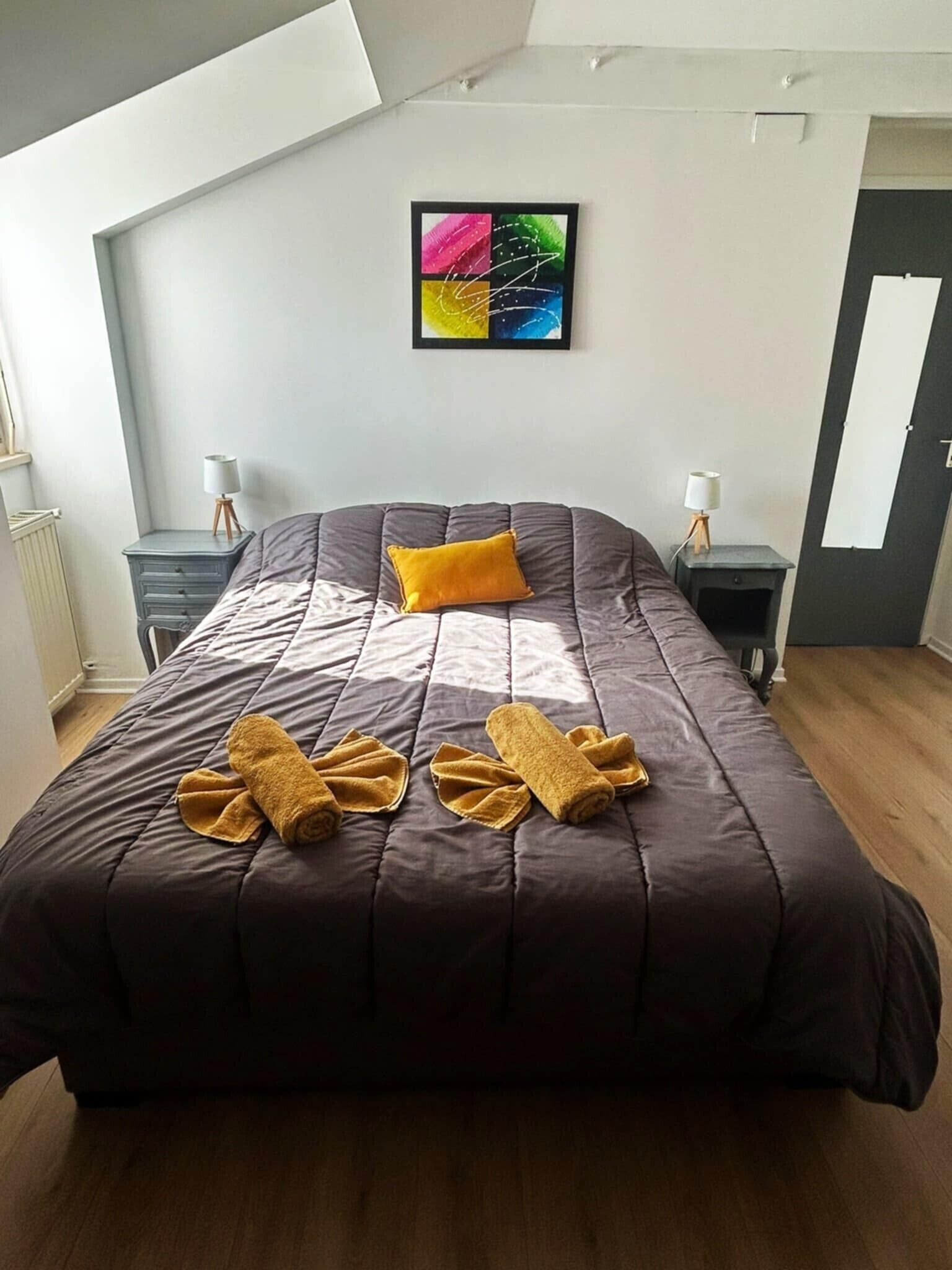 Una camera da letto moderna con un letto grande, un quadro astratto dai colori vivaci e un velux.