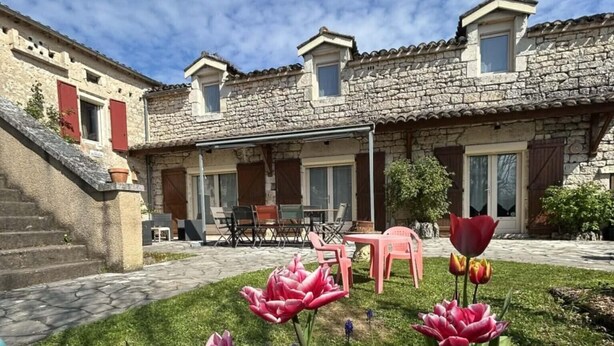 Une cour bordée de bâtiments en pierre, une pelouse et quelques tulipes roses.