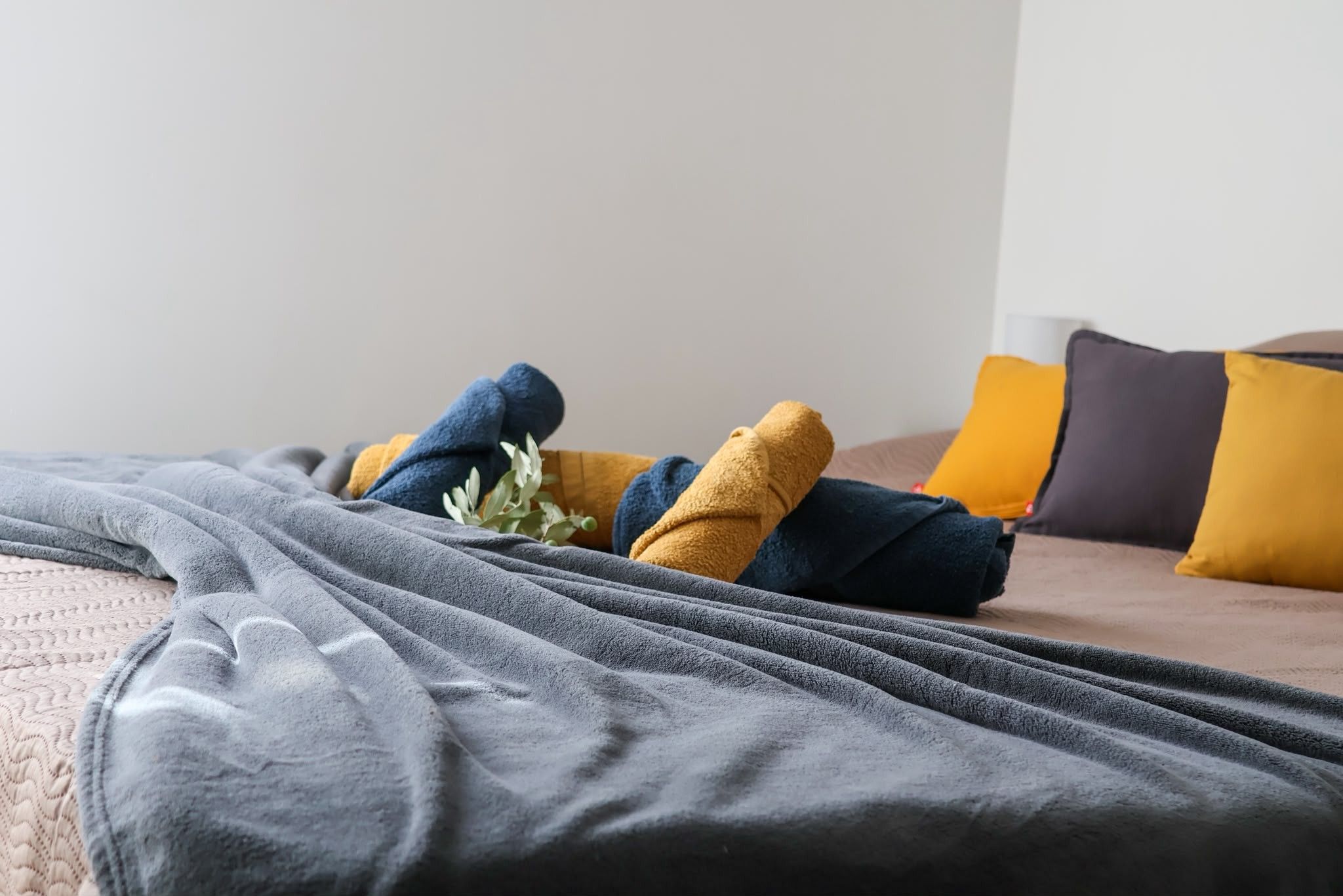 Un lit avec une couverture grise et plusieurs oreillers de différentes couleurs.