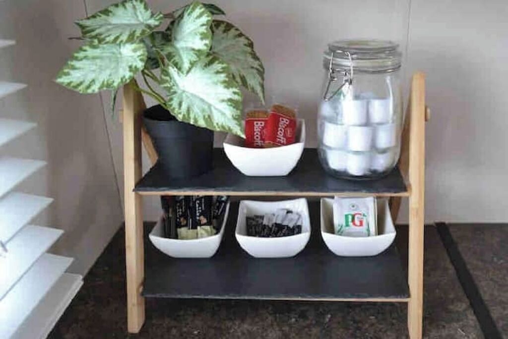 A shelf with a potted plant, a jar of sugar, and several white bowls containing various items.