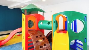 Un'area giochi al coperto colorata, con uno scivolo, una struttura di arrampicata e un tunnel.