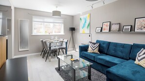 Una sala de estar moderna con un sofá azul, una mesa de centro de vidrio y un comedor con mesa y sillas.