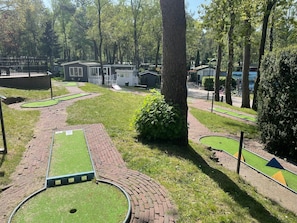 Ein Minigolfplatz mit grünem Rasen, Ziegelwegen und einem kleinen Gebäude im Hintergrund.