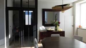 A modern dining area with a large table, a dark wooden cabinet with decorative items, a mirror, and a sliding glass door leading to another room. - "Le Clos Lesage", charming house with garden, at the foot of the chateau (Dinan)