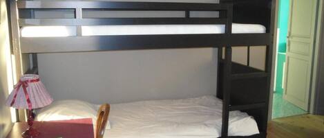 A bunk bed with a desk and chair, a lamp, and a door in the background.