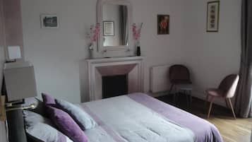 Un dormitorio con cama, una silla, chimenea y espejo.