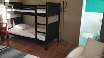 A bunk bed with a chair and a desk, a coat rack, and a bathroom visible in the background.