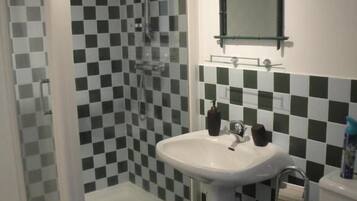 A bathroom with a checkered tile wall, a white pedestal sink, a glass-enclosed shower, and a toilet.