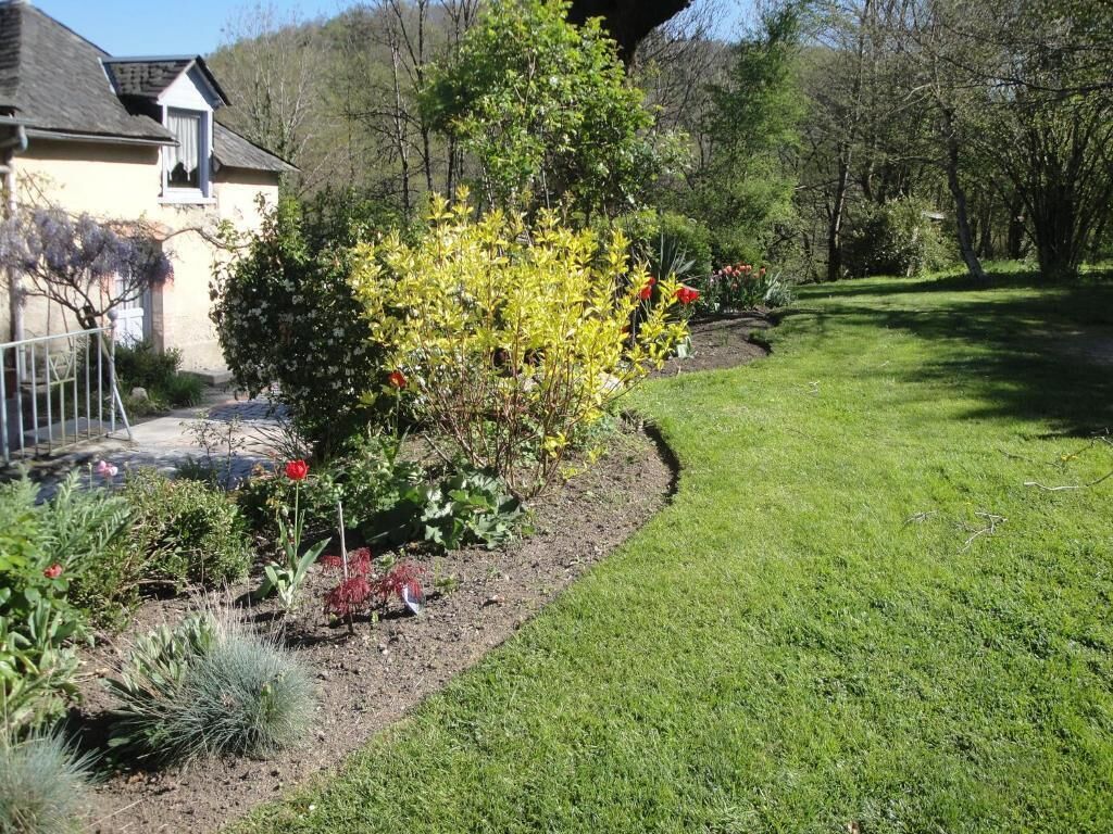 A well-maintained garden with a variety of plants and flowers, a neatly trimmed lawn, and a house with a sloped roof and a visible window.