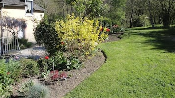 A well-maintained garden with a variety of plants and flowers, a neatly trimmed lawn, and a house with a sloped roof and a visible window.