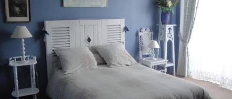 A bedroom with a bed, a nightstand, a lamp, a vase with flowers, and a window with curtains.