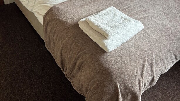 Un lit bien fait, avec une tête de lit beige, une couette blanche et deux oreillers beige.
