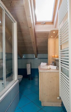 A narrow bathroom with a skylight, wooden ceiling, and blue-tiled floor.