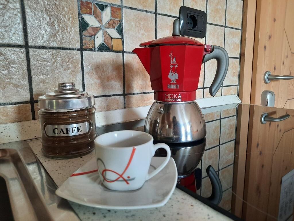 Eine Küchenarbeitsplatte mit einer Kaffeemaschine, einem mit „CAFFE“ beschrifteten Einmachglas und einer Tasse auf Untertasse.