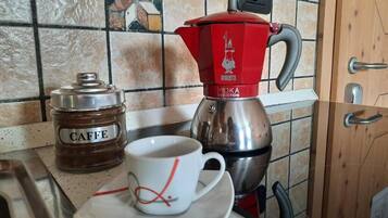 Eine Küchenarbeitsplatte mit einer Kaffeemaschine, einem mit „CAFFE“ beschrifteten Einmachglas und einer Tasse auf Untertasse.