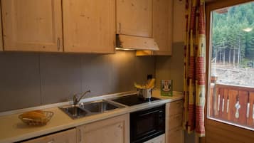 Una cocina con armarios de madera, un fregadero, una estufa y una ventana con vistas a árboles.