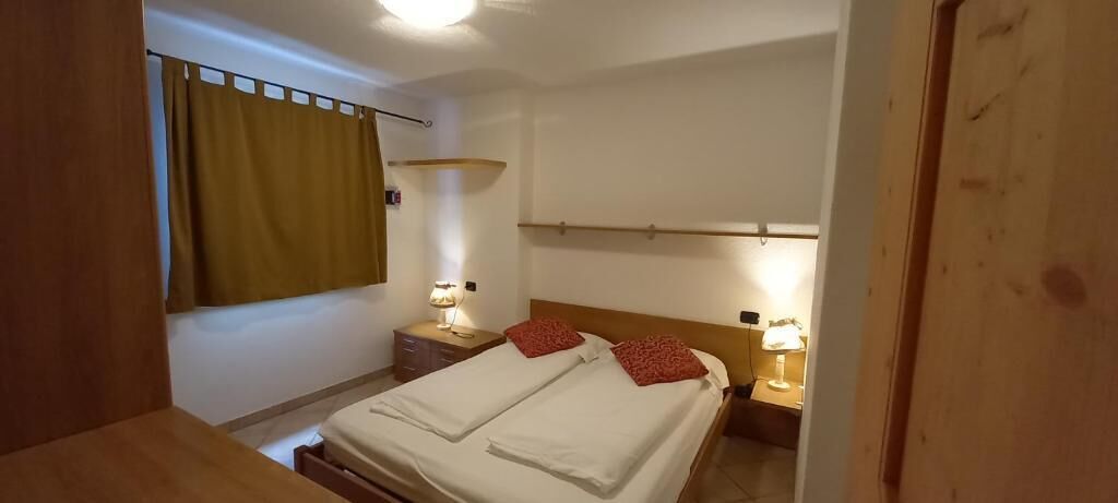 Een slaapkamer met twee bedden, een houten hoofdbord, nachtlampjes en een raam met gordijnen.