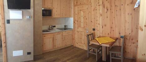 Una cocina compacta con armarios de madera, un microondas y un lavamanos. Hay un pequeño comedor con una mesa y sillas.