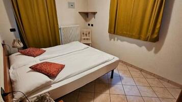 Une chambre avec un lit simple, une table de chevet en bois, une petite table, un radiateur et des rideaux jaunes.