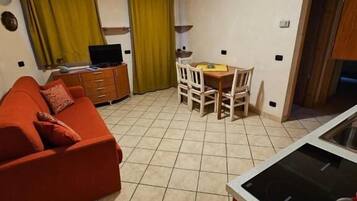 Un espacio habitable compacto con sofá, una mesa de comedor con sillas, televisor y kitchenette.