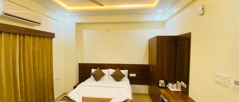 A hotel room with a bed, a desk, a mirror, and a ceiling fan.