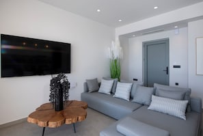 A modern living room with a grey sofa, a wooden coffee table, and a large flat-screen TV mounted on the wall. - Luxury villa with kingsize beds and breathtaking sea view ( El paradiso villa) (Akrotiri)