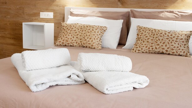 Een opgemaakt bed met witte en gemêleerde kussens, een witte nachtkastje en een houten hoofdbord.